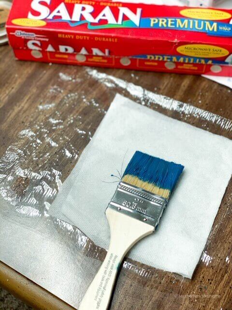 Paint brush covered in DIY chalk paint being wrapped in saran wrap for use later