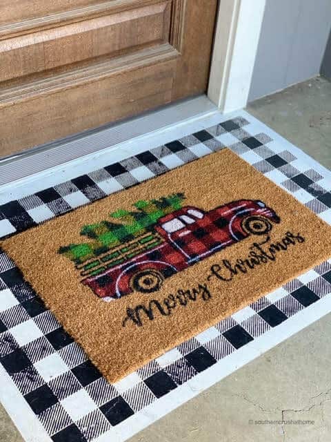 Christmas doormat with plaid truck layered on top of a painted buffalo check doormat