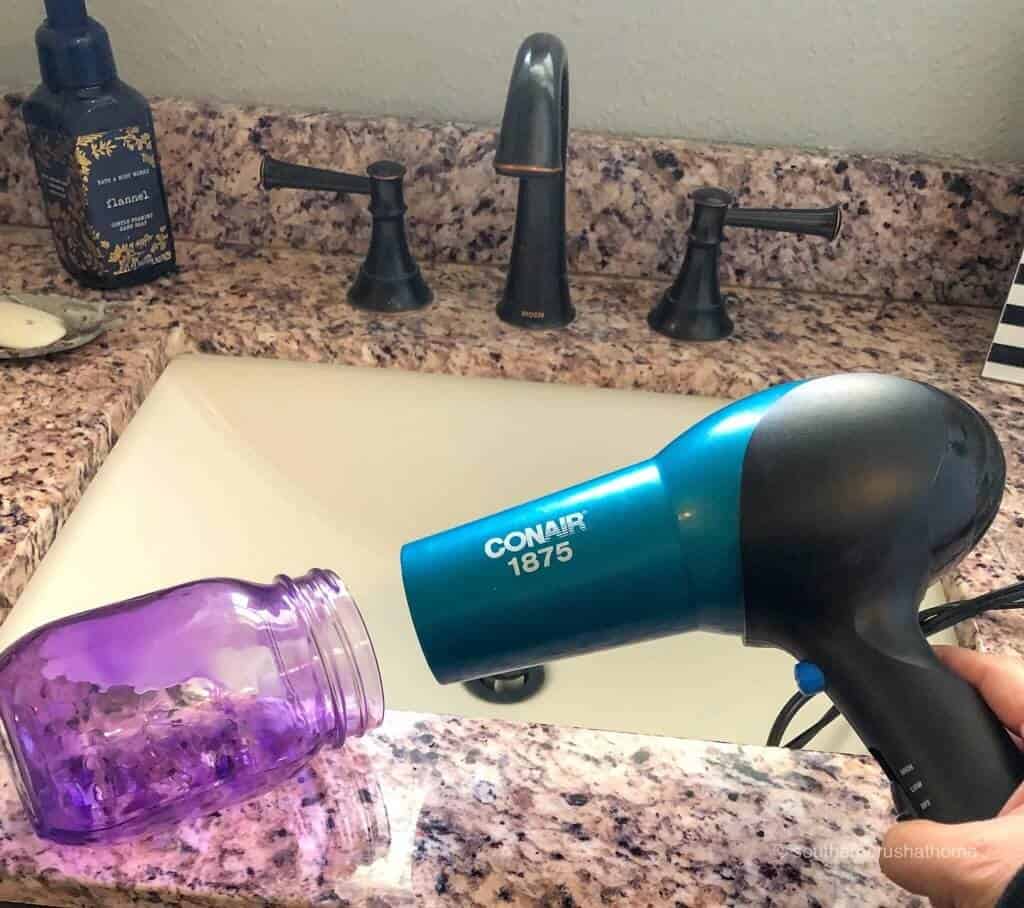 Using a hair dryer to dry the inside of a purple-stained mason jar