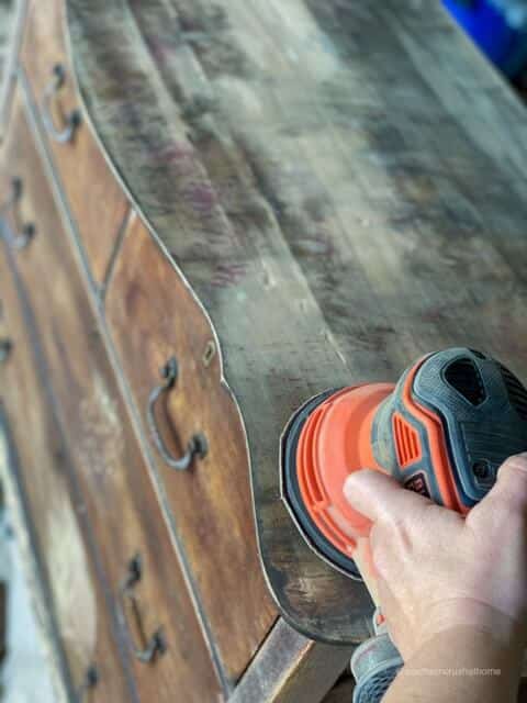 Using a sander to sand the top of an old dresser 