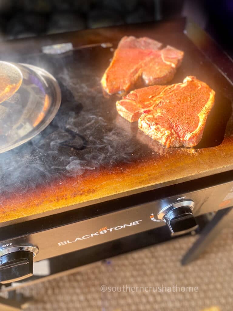 two porterhouse steaks cooking on a Blackstone griddle