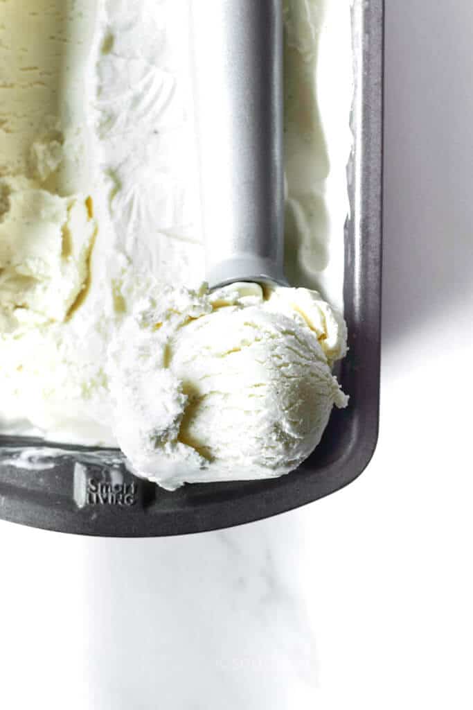 scooping homemade vanilla ice cream from a loaf pan