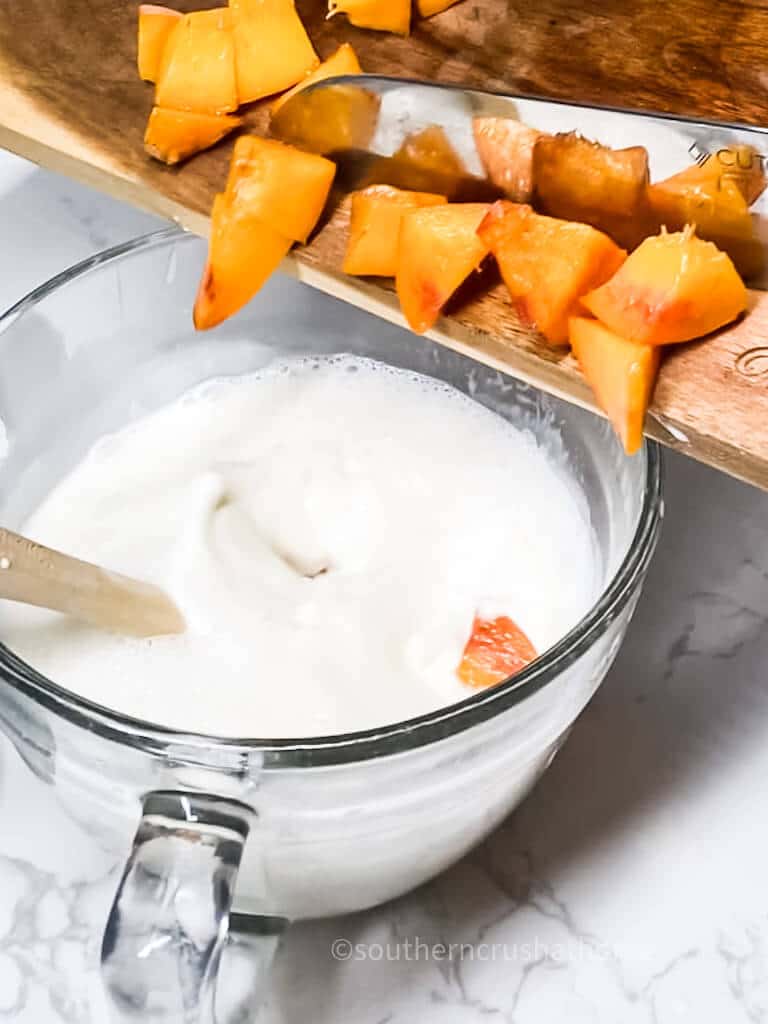 pouring chopped peaches into cream