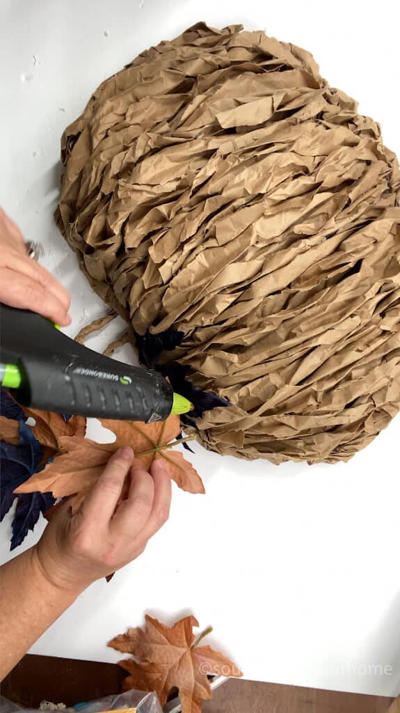 gluing on faux leaves to pumpkin wreath