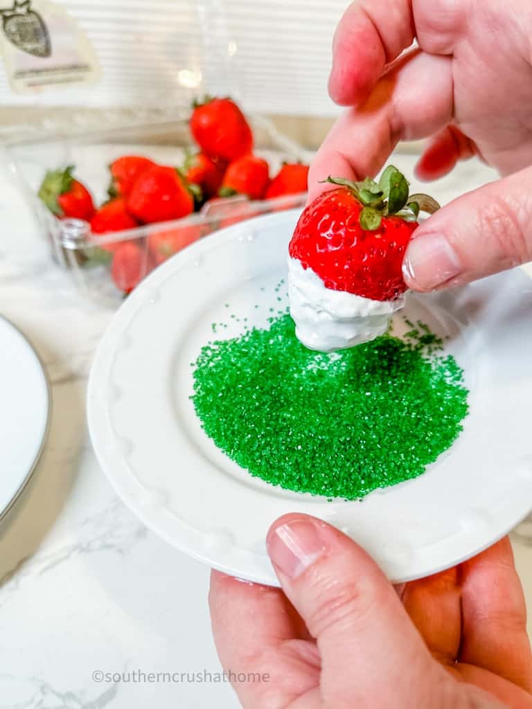 dipping a strawberry into green sprinkles