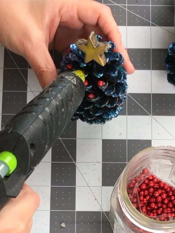 hot gluing red berries onto pine cone