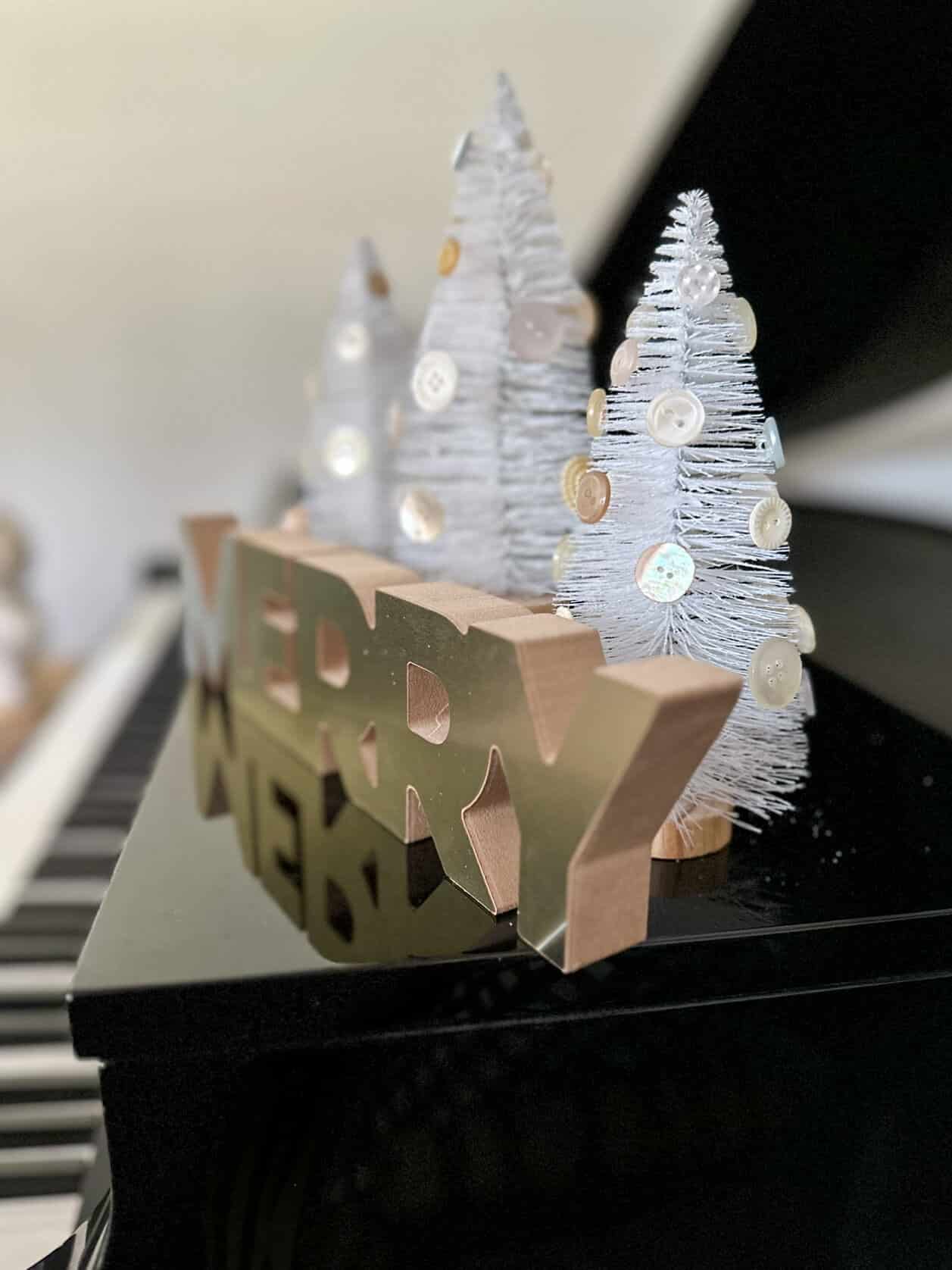 bottle brush trees on piano with merry sign