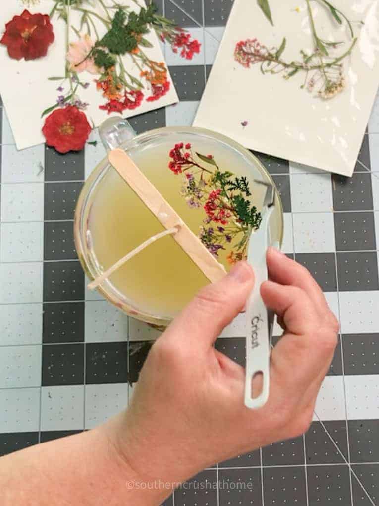 using tweezer tool to place dried flowers on top of candle wax
