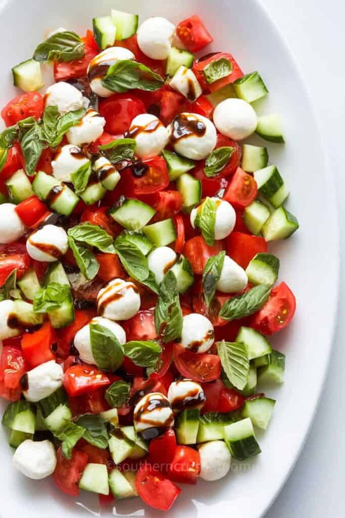 A beautifully arranged Cucumber Caprese Salad with slices of cucumber, tomato, and mozzarella, garnished with fresh basil.