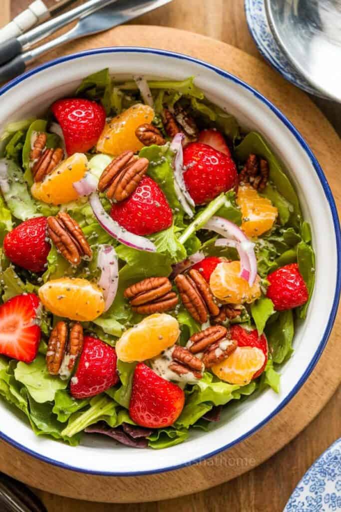 A vibrant Summer Strawberry Salad with greens, strawberries, pecans, and dressing.